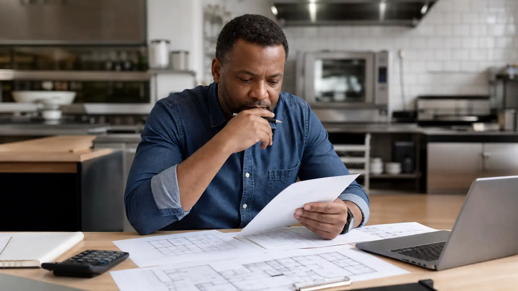A South African food service business owner reviewing commercial kitchen cost estimates and floor plans